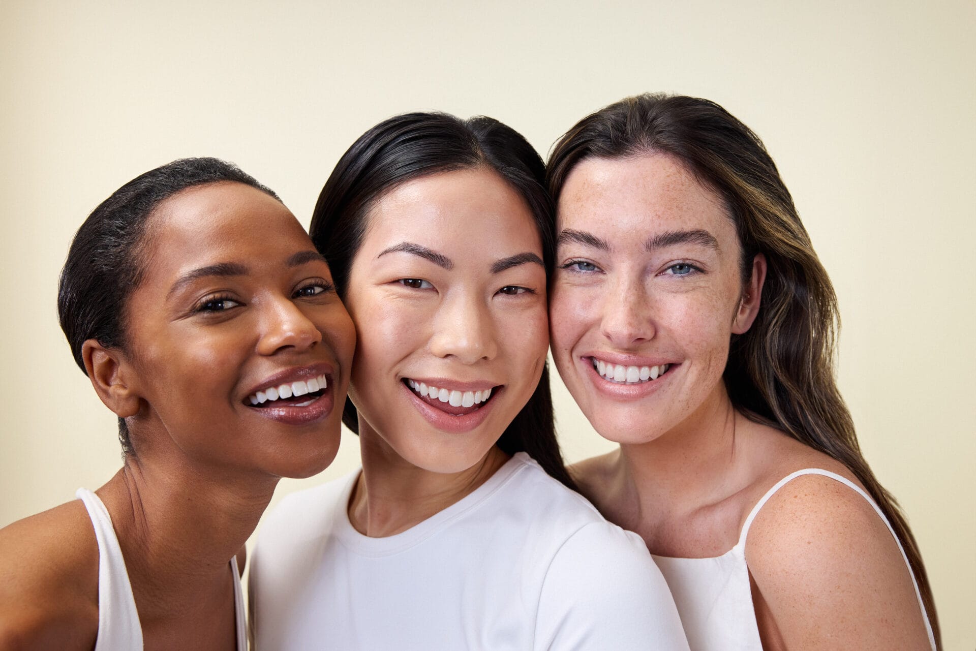 Three people smiling, close together, against a plain background.